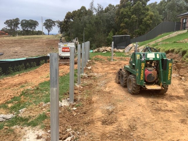 Steel retaining wall posts and compact machinery during construction