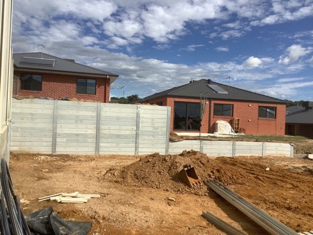 Concrete sleeper retaining wall being installed beside an Albury-style brick home
