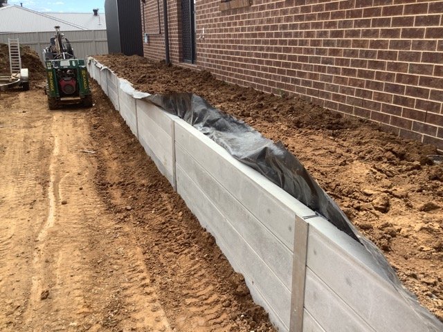 Concrete sleeper retaining wall beside a brick home during construction