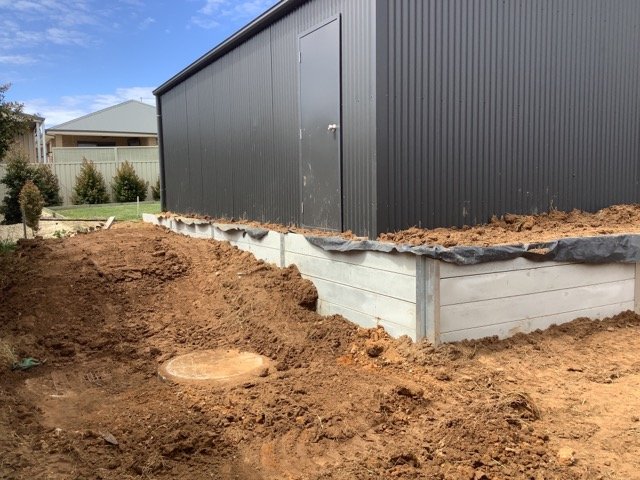 Concrete sleeper retaining wall wrapping around a residential building