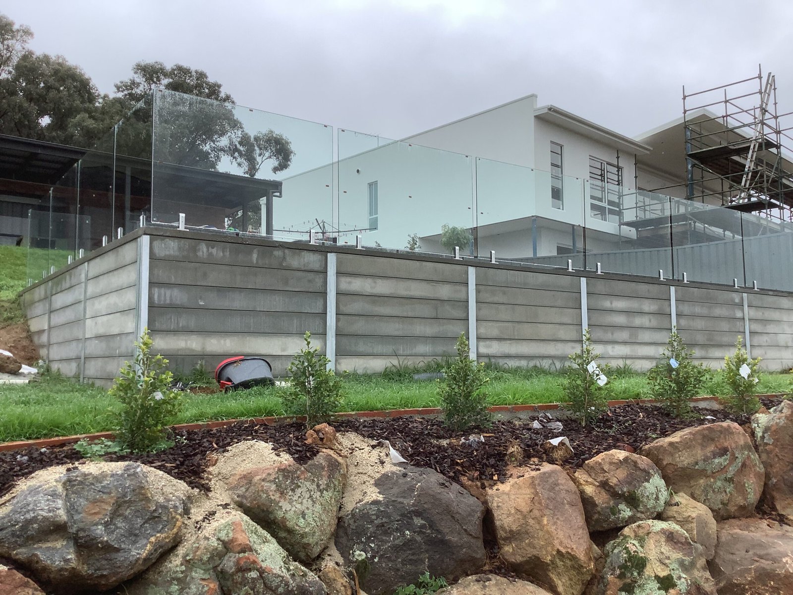 Finished concrete sleeper retaining wall with glass balustrade and landscaping