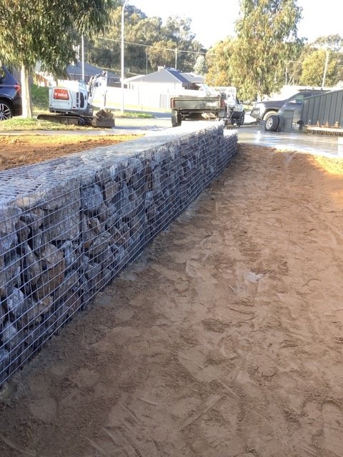 Long completed gabion retaining wall beside a residential property