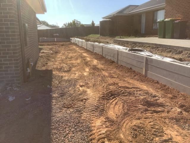 Concrete sleeper retaining wall with shaped ground beside a home